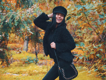 Portrait of smiling young woman standing in forest during autumn