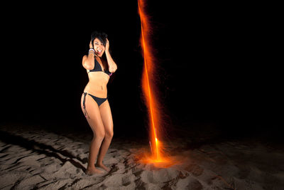 Woman in bikini playing with firework on beach at night