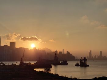 Scenic view of sea and silhouette buildings against sky during sunset