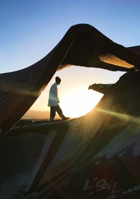 Side view of man walking on land seen through metallic structure against sky during sunset