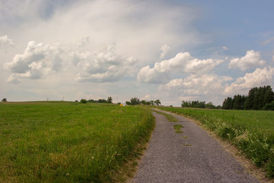 Empty road amidst field against sky