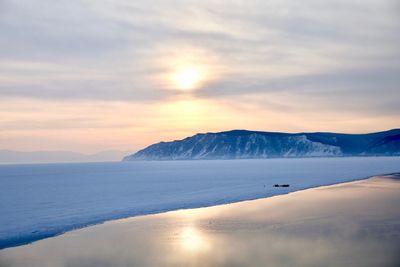 Scenic view of snowcapped mountains by sea against sky during sunset