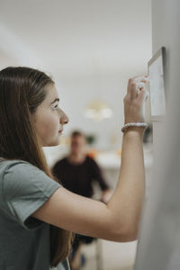 Side view of girl using home automation app through digital tablet mounted on wall