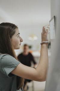 Side view of girl using home automation app through digital tablet mounted on wall