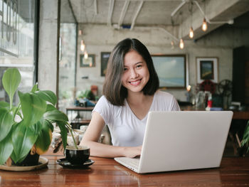 Portrait of smiling young businesswoman using laptop on table at cafe