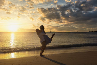 Full length of woman standing at beach against sky during sunset