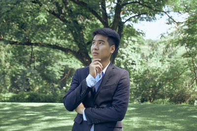 Young man looking away while standing on tree