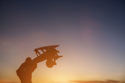 Silhouette man holding toy while standing against sky during sunset