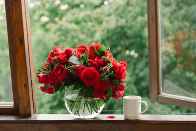 Bouquet of red rose in a vase and a book on a wooden window sill.
