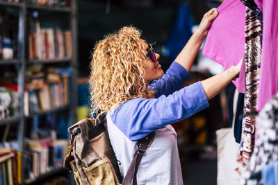 Side view of woman with backpack choosing cloth at market