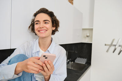 Portrait of young woman using mobile phone while sitting on table