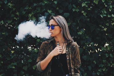 Young woman looking away while standing by tree