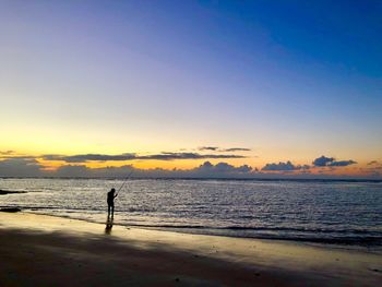 Silhouette fishing at beach against sky during sunset