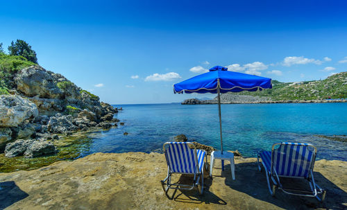 Parasol and deck chairs at beach against blue sky