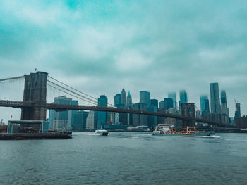 Bridge over river by buildings against sky in city