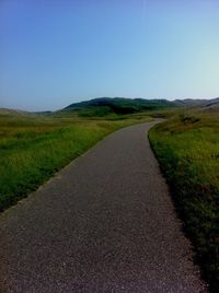 Road passing through field against blue sky