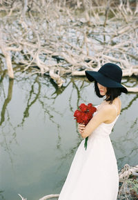 Woman in hat with bouquet standing against lake