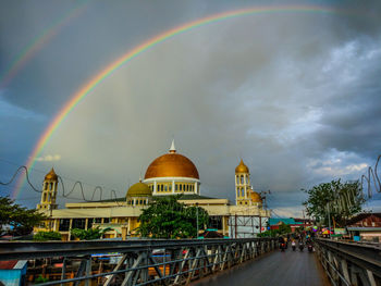 Rainbow over city against cloudy sky