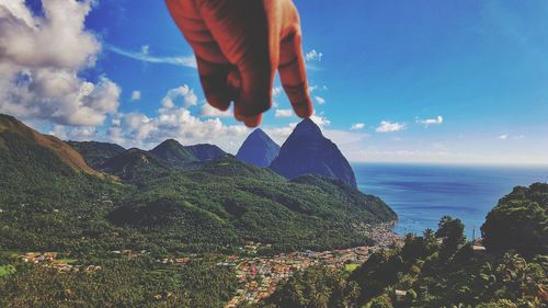 Optical illusion of cropped hand touching mountain peak by sea