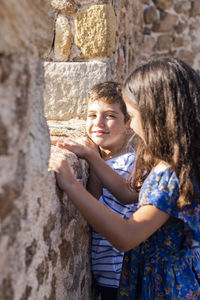 Siblings standing by stone wall