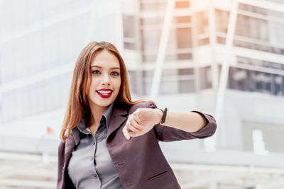 Portrait of smiling young businesswoman checking time while standing on elevated walkway 