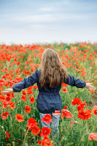 Rear view of woman standing by flowers on field