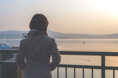 Rear view of woman standing against sea during sunset