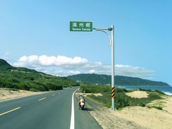 Road sign on street against sky