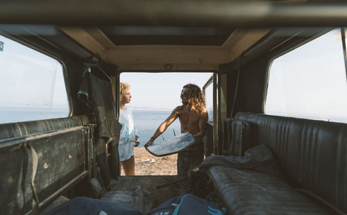 Man removing surfboard while talking with woman at beach