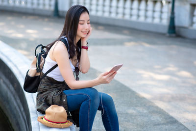 Young woman using mobile phone while sitting in city