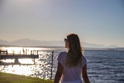 Rear view of woman standing on beach against clear sky