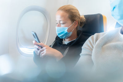 A young woman wearing face mask, using smart phone while traveling on airplane. new normal travel