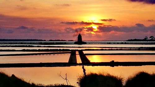 Silhouette built structure by sea against sky during sunset