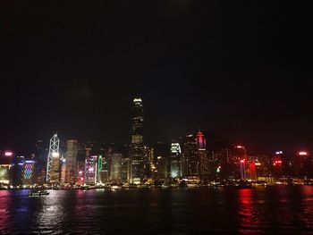 Illuminated buildings by river against sky at night