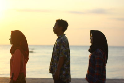 People standing on beach against sky during sunset