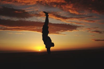 Silhouette man standing on rock against sky during sunset