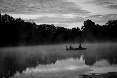 Silhouette people on boat in lake against sky