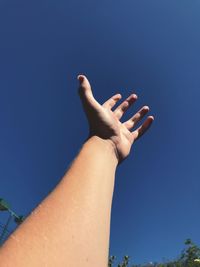 Low angle view of hand against clear blue sky