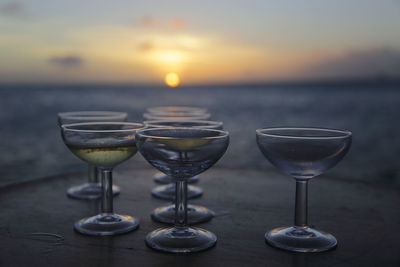 Close-up of wine glasses on table against sea during sunset