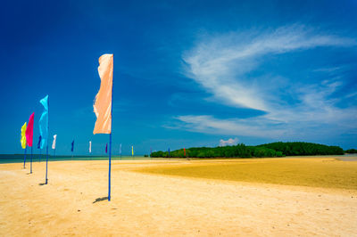 Flags at sandy beach against blue sky