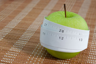 Close-up of tape measure rolled up on apple over table