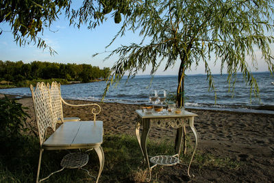 Empty chairs and table at beach against sky