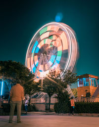People by illuminated ferris wheel against sky at night