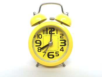 Close-up of yellow clock over white background