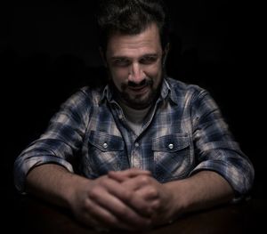 Portrait of man sitting against black background