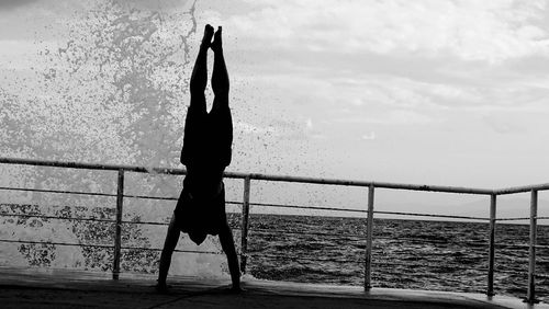 Full length of silhouette man practicing handstand by sea against sky