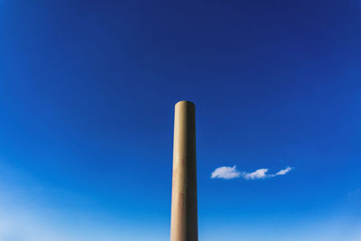 Low angle view of smoke emitting from chimney against blue sky