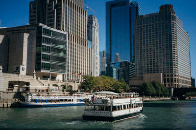 Boat in river by buildings against sky in city