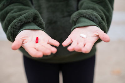 Midsection of woman with red and white pill standing on road