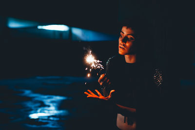 Woman holding lit sparkler in darkroom